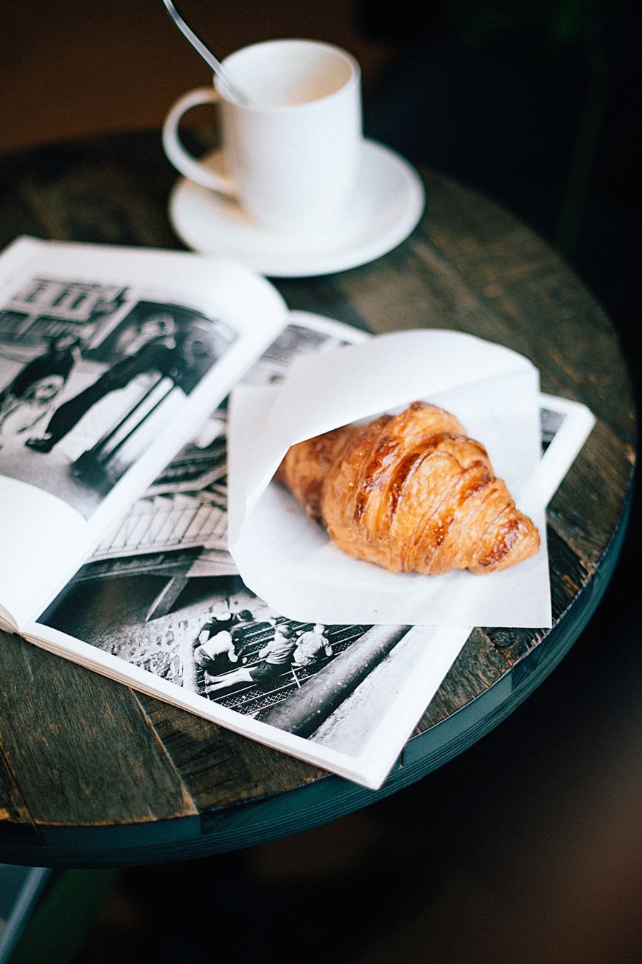A croissant and coffee on a dark wooden cafe table